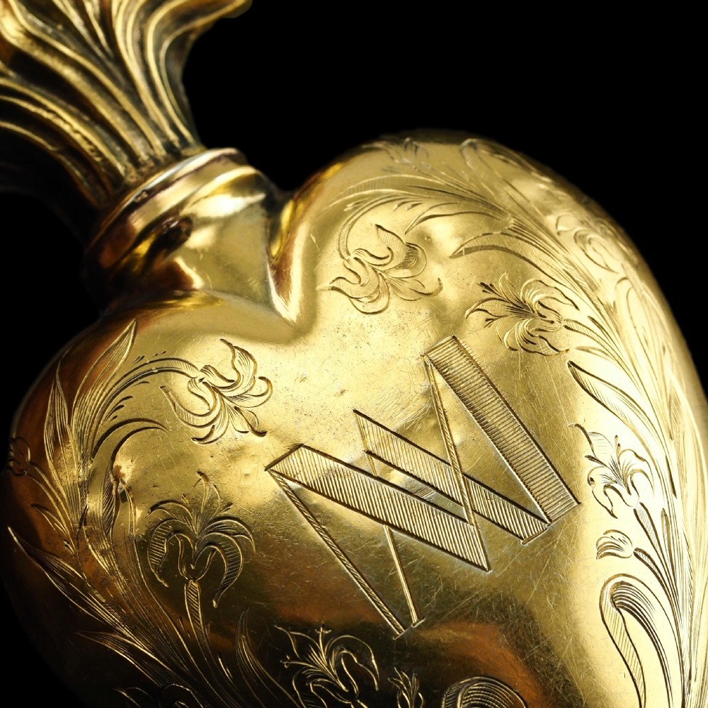 A 19th-century French silver-gilt heart-shaped scent bottle featuring an engraved monogram, foliate scrollwork, and a flame-shaped stopper. View XVI