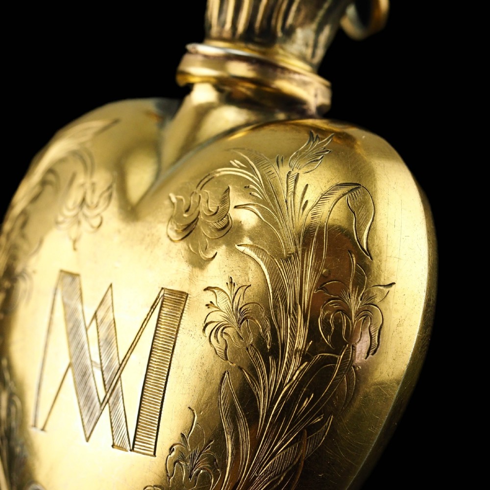 A 19th-century French silver-gilt heart-shaped scent bottle featuring an engraved monogram, foliate scrollwork, and a flame-shaped stopper. View XX