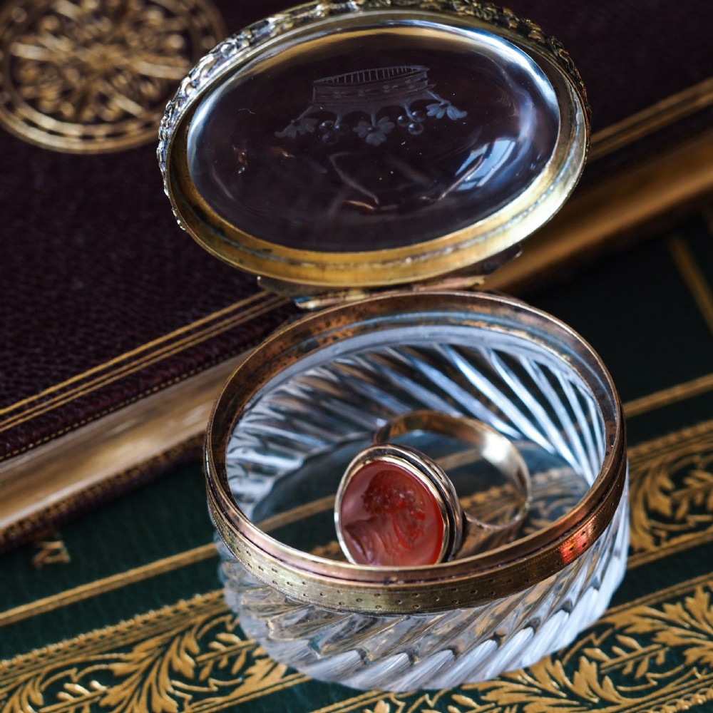An oval cut crystal box featuring a gilt silver rim and a transparent glass lid etched with a nobility coronet crest. View X