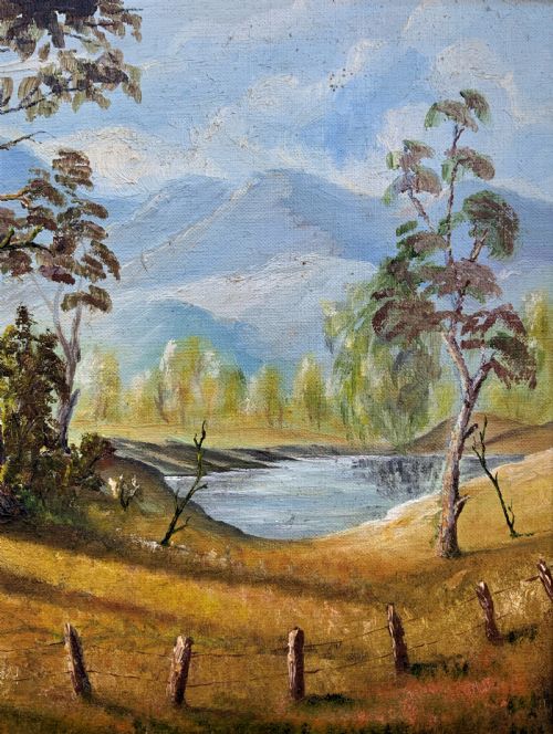 fig 4. A mid-century oil landscape painting depicting tall gum trees beside a lake against blue mountains, framed in a gilt and fabric-lined wooden frame.