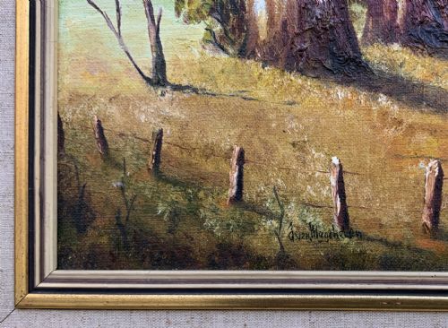 fig 7. A mid-century oil landscape painting depicting tall gum trees beside a lake against blue mountains, framed in a gilt and fabric-lined wooden frame.