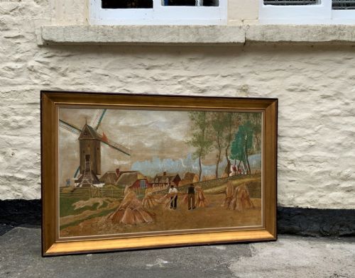 fig 1. A mid-20th-century naive oil painting depicting agricultural workers gathering hay bales in a field beside a timber windmill, thatched cottages, and trees, presented in a gilt frame.