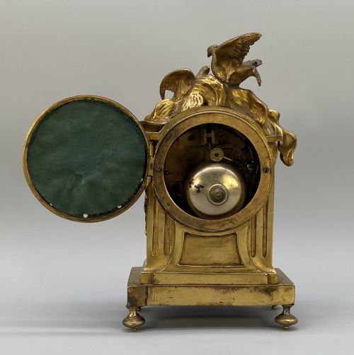 fig 5. An antique French gilt bronze mantel clock surmounted by two sculpted doves, featuring an ornate pedestal base and a white enamel dial with Roman numerals.