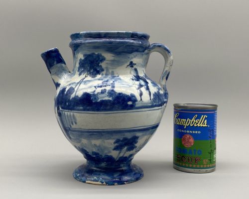 fig 2. An 18th-century Italian Savona majolica wet drug jar featuring hand-painted cobalt blue landscapes, a single side handle, a raised spout, and a pedestal base.