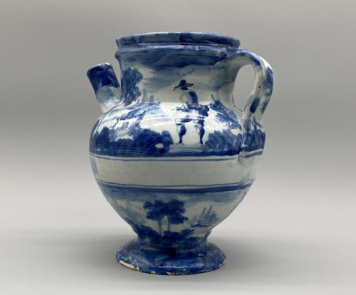 fig 3. An 18th-century Italian Savona majolica wet drug jar featuring hand-painted cobalt blue landscapes, a single side handle, a raised spout, and a pedestal base.