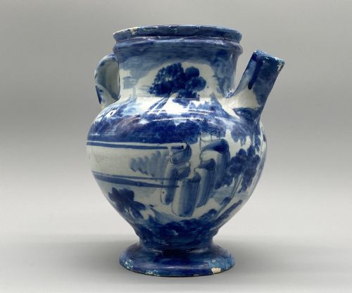 fig 6. An 18th-century Italian Savona majolica wet drug jar featuring hand-painted cobalt blue landscapes, a single side handle, a raised spout, and a pedestal base.