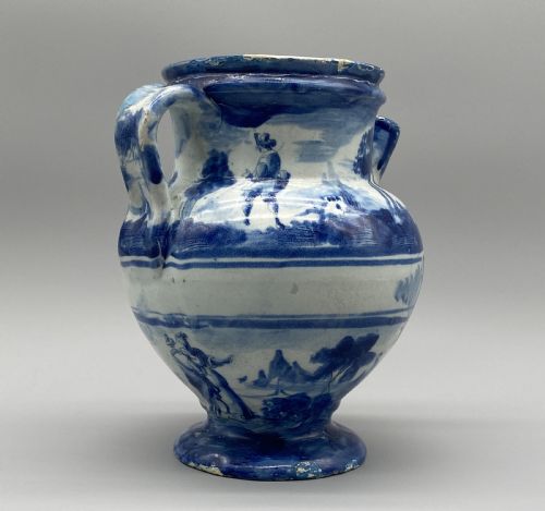 fig 7. An 18th-century Italian Savona majolica wet drug jar featuring hand-painted cobalt blue landscapes, a single side handle, a raised spout, and a pedestal base.