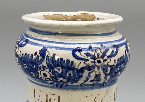 fig 4. An 18th-century Italian majolica albarello pharmacy jar featuring a waisted silhouette with hand-painted blue floral patterns and central apothecary inscription.