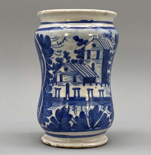 fig 1. A cylindrical tin-glazed earthenware albarello jar with a waisted body featuring hand-painted blue scrollwork and the date 1709 on a cream-white background.