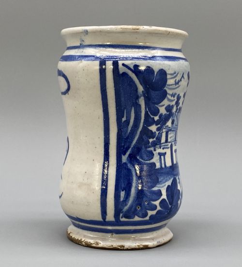 fig 5. A cylindrical tin-glazed earthenware albarello jar with a waisted body featuring hand-painted blue scrollwork and the date 1709 on a cream-white background.