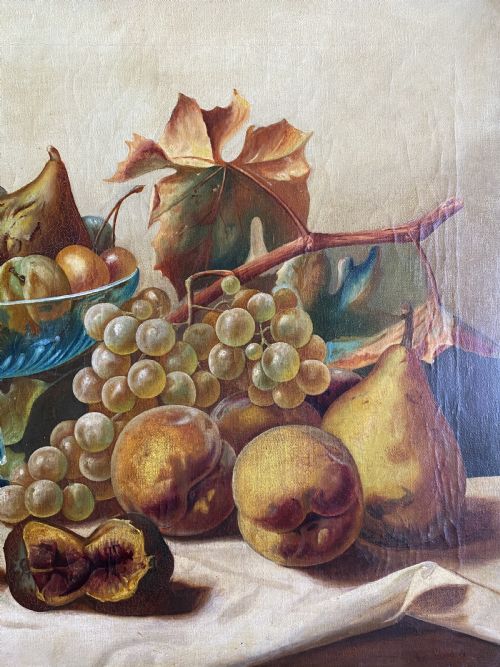 fig 3. An oil painting depicting a still life composition of grapes, pears, peaches, and figs arranged on a draped cloth with a blue glass pedestal dish, enclosed in a moulded gilt frame.