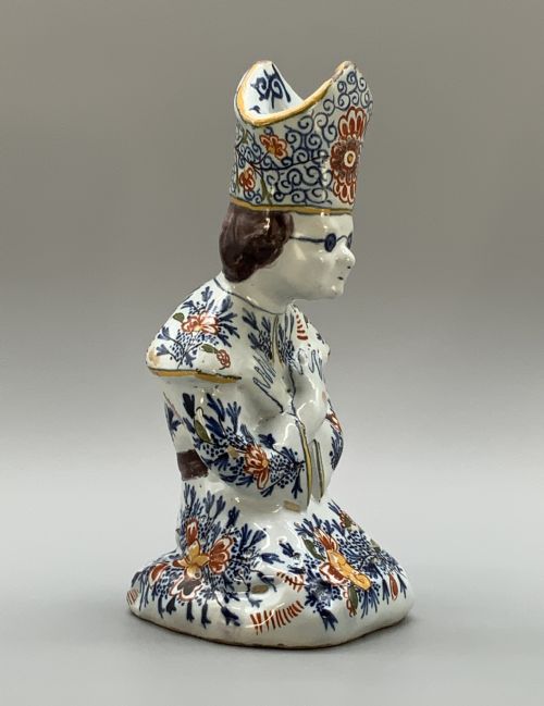 fig 2. An 18th-century Dutch Delftware ceramic candlestick formed as a kneeling bishop in patterned robes and a mitre decorated with polychrome glazes.