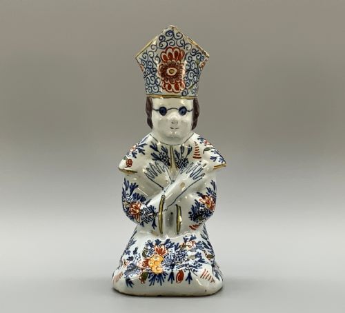 fig 3. An 18th-century Dutch Delftware ceramic candlestick formed as a kneeling bishop in patterned robes and a mitre decorated with polychrome glazes.