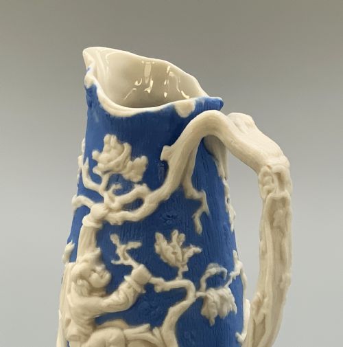 fig 2. A Victorian blue and white Parian ware jug featuring a textured cobalt blue ground with raised white relief figures climbing a tree and a moulded branch handle.