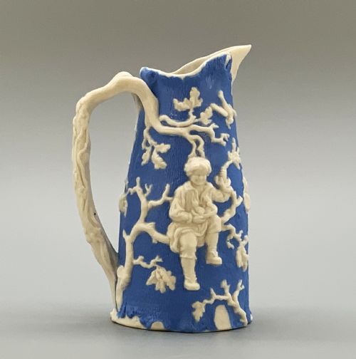 fig 5. A Victorian blue and white Parian ware jug featuring a textured cobalt blue ground with raised white relief figures climbing a tree and a moulded branch handle.