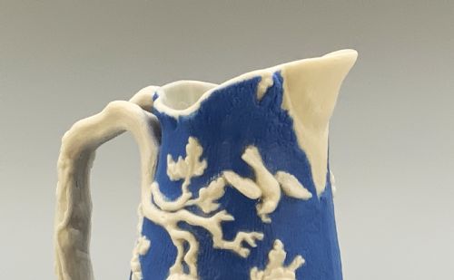 fig 7. A Victorian blue and white Parian ware jug featuring a textured cobalt blue ground with raised white relief figures climbing a tree and a moulded branch handle.