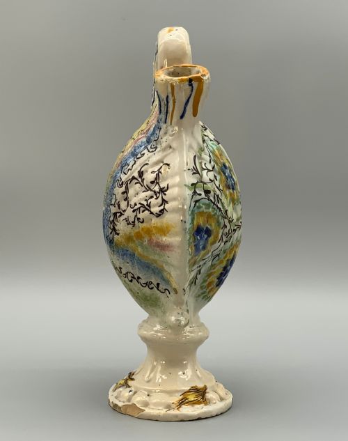 fig 3. An 18th-century Italian polychrome majolica pilgrim flask formed as a scallop shell with an overhead handle, side loops, and hand-painted floral motifs in blue, yellow, and green over a cream glazed surface.