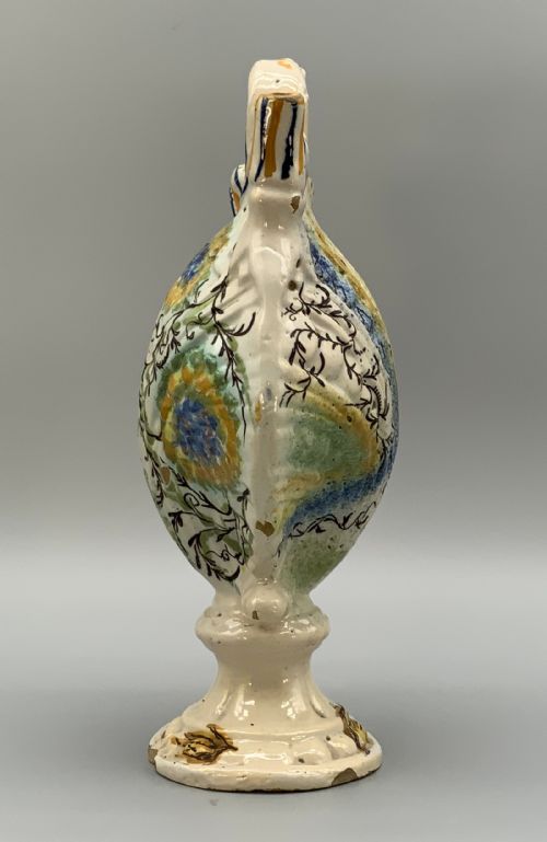 fig 4. An 18th-century Italian polychrome majolica pilgrim flask formed as a scallop shell with an overhead handle, side loops, and hand-painted floral motifs in blue, yellow, and green over a cream glazed surface.
