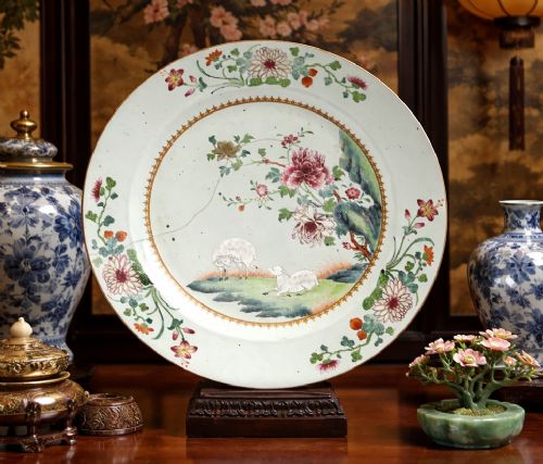 fig 6. A large circular Chinese export porcelain charger plate hand-painted with famille rose floral motifs, rockwork, and two white sheep on a pale background.