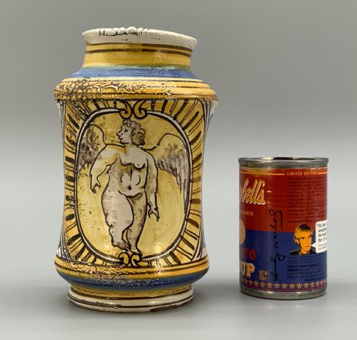 fig 2. A waisted cylindrical tin-glazed majolica albarello jar decorated in yellow, blue, and dark brown hand-painted pigments featuring a central winged figure motif.