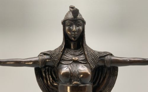 fig 4. A patinated bronze Egyptian Revival candelabra featuring a female figure with outstretched arms holding two candle sockets, standing on a decorated triangular base.