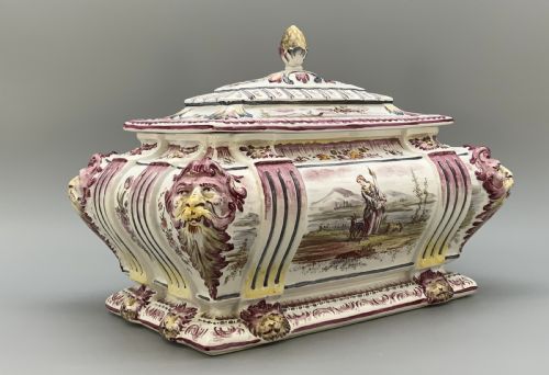 fig 3. An antique French faience covered soup tureen featuring hand-painted pastoral scenes in manganese purple, moulded lion mask side handles, and a stepped lid with a finial.