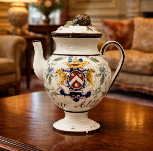 fig 1. An 18th-century Italian tin-glazed earthenware pharmacy wet drug jug with a spouted body, top handle, lid with sculpted finial, painted armorial crest, floral scrolls, and Latin text reading Syr Alth.