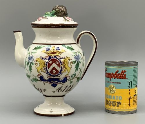 fig 2. An 18th-century Italian tin-glazed earthenware pharmacy wet drug jug with a spouted body, top handle, lid with sculpted finial, painted armorial crest, floral scrolls, and Latin text reading Syr Alth.