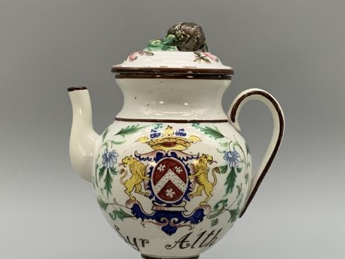 fig 3. An 18th-century Italian tin-glazed earthenware pharmacy wet drug jug with a spouted body, top handle, lid with sculpted finial, painted armorial crest, floral scrolls, and Latin text reading Syr Alth.