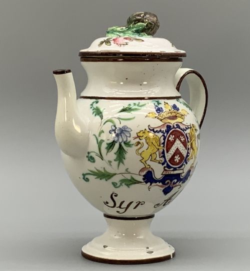 fig 4. An 18th-century Italian tin-glazed earthenware pharmacy wet drug jug with a spouted body, top handle, lid with sculpted finial, painted armorial crest, floral scrolls, and Latin text reading Syr Alth.
