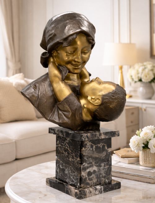 fig 1. A two-tone bronze bust of a mother wearing a headscarf cradling her infant, mounted on a tall rectangular black veined marble pedestal.