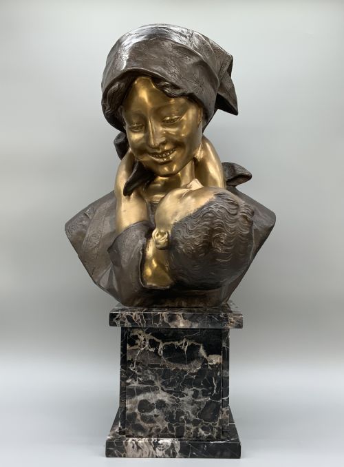 fig 2. A two-tone bronze bust of a mother wearing a headscarf cradling her infant, mounted on a tall rectangular black veined marble pedestal.