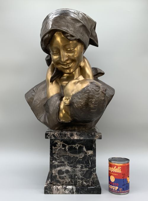 fig 3. A two-tone bronze bust of a mother wearing a headscarf cradling her infant, mounted on a tall rectangular black veined marble pedestal.