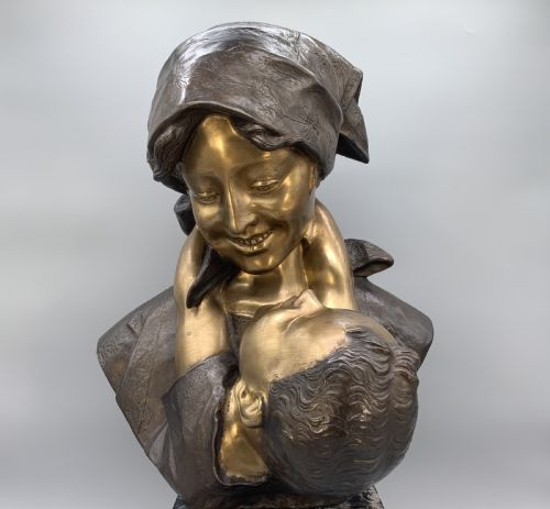 fig 4. A two-tone bronze bust of a mother wearing a headscarf cradling her infant, mounted on a tall rectangular black veined marble pedestal.