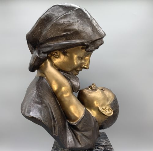 fig 5. A two-tone bronze bust of a mother wearing a headscarf cradling her infant, mounted on a tall rectangular black veined marble pedestal.