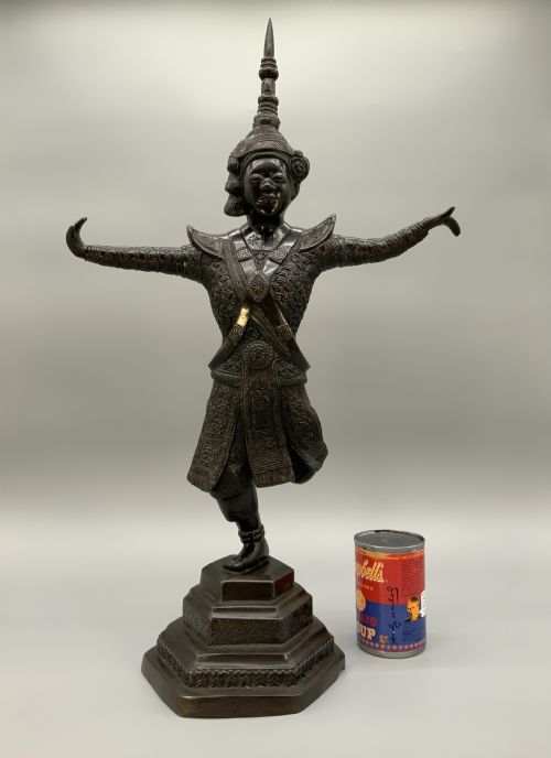 fig 2. A dark bronze sculpture depicting a classical court dancer in ceremonial attire with a tall spired headdress, balanced on one foot atop an octagonal stepped base.