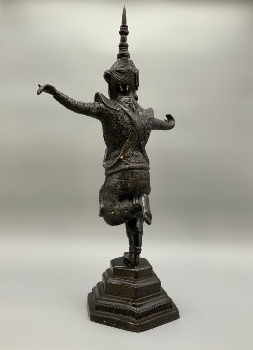 fig 5. A dark bronze sculpture depicting a classical court dancer in ceremonial attire with a tall spired headdress, balanced on one foot atop an octagonal stepped base.