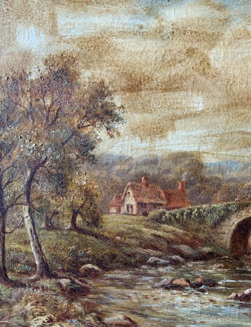 fig 6. An antique oil painting depicting a tranquil river flowing through a wooded landscape with a stone bridge and cottage in the background, framed in polished dark wood.