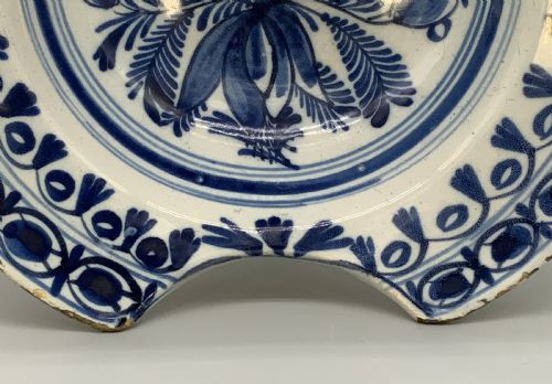 fig 5. An 18th-century blue and white Dutch Delftware barbers bowl featuring hand-painted floral motifs and a semi-circular rim notch.