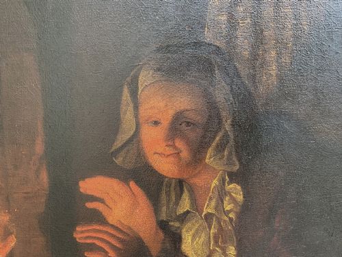 fig 5. A framed oil painting depicting a woman in historic dress warming her hands beside a glowing fire in a darkened interior.
