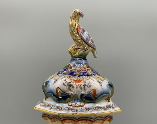 fig 7. A pair of ornate French faience lidded vases decorated with hand-painted polychrome florals, Rococo scrollwork moulding, and sculptural parrot finials.
