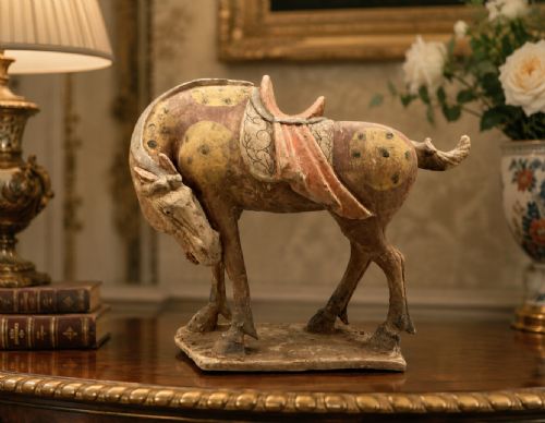 fig 1. A terracotta horse figurine featuring a dappled coat pattern, draped saddle, and a head lowered towards its front hoof on a rectangular plinth.