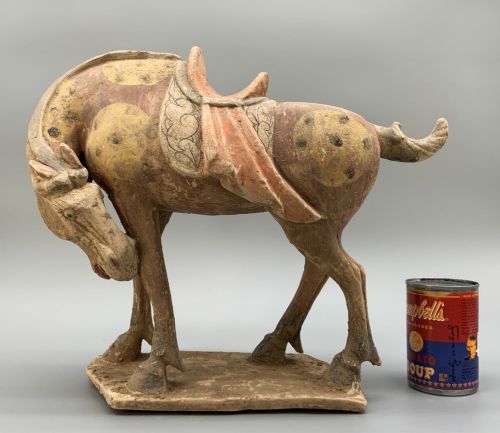 fig 2. A terracotta horse figurine featuring a dappled coat pattern, draped saddle, and a head lowered towards its front hoof on a rectangular plinth.