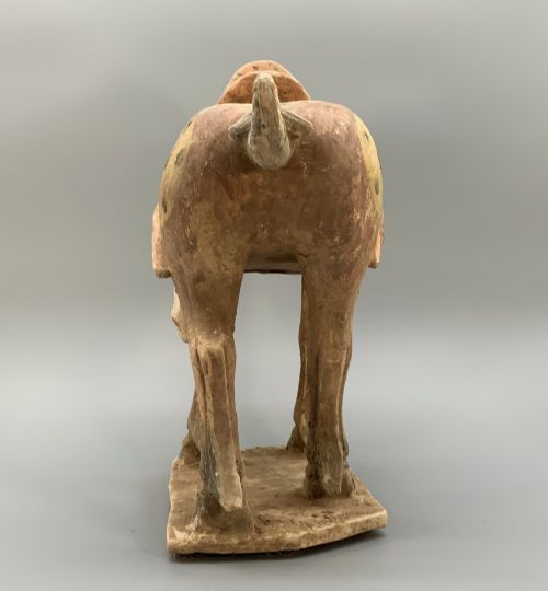 fig 4. A terracotta horse figurine featuring a dappled coat pattern, draped saddle, and a head lowered towards its front hoof on a rectangular plinth.
