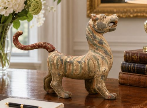 fig 1. A painted earthenware figure of a tiger-like mythical beast from the Han Dynasty featuring an arched neck, raised tail, and red and green painted stripes.