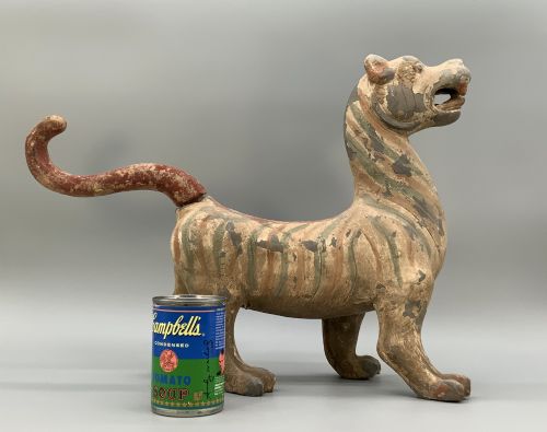 fig 2. A painted earthenware figure of a tiger-like mythical beast from the Han Dynasty featuring an arched neck, raised tail, and red and green painted stripes.