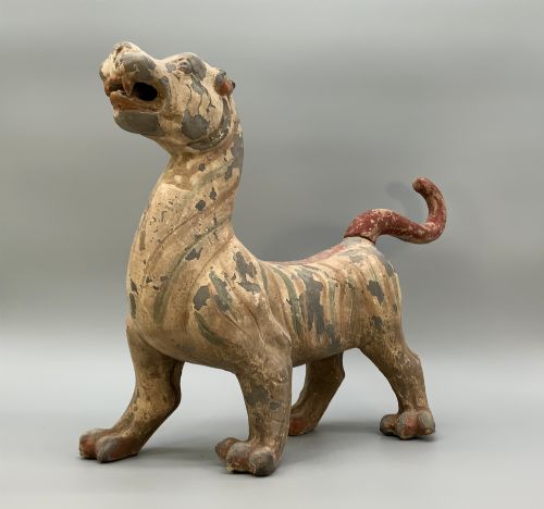 fig 3. A painted earthenware figure of a tiger-like mythical beast from the Han Dynasty featuring an arched neck, raised tail, and red and green painted stripes.