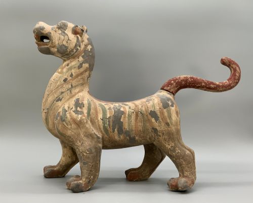 fig 4. A painted earthenware figure of a tiger-like mythical beast from the Han Dynasty featuring an arched neck, raised tail, and red and green painted stripes.