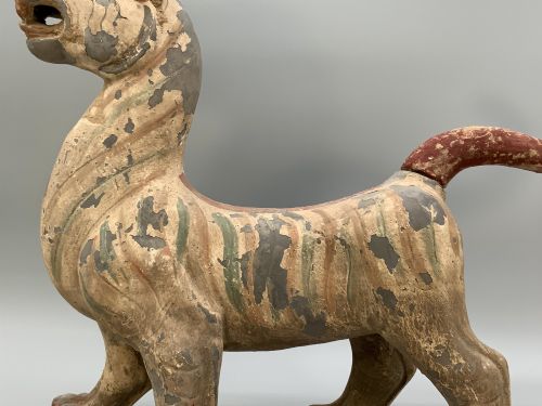 fig 6. A painted earthenware figure of a tiger-like mythical beast from the Han Dynasty featuring an arched neck, raised tail, and red and green painted stripes.