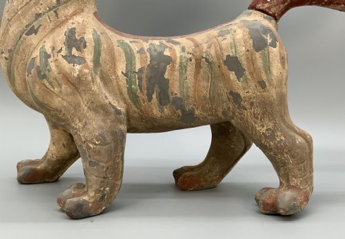 fig 7. A painted earthenware figure of a tiger-like mythical beast from the Han Dynasty featuring an arched neck, raised tail, and red and green painted stripes.